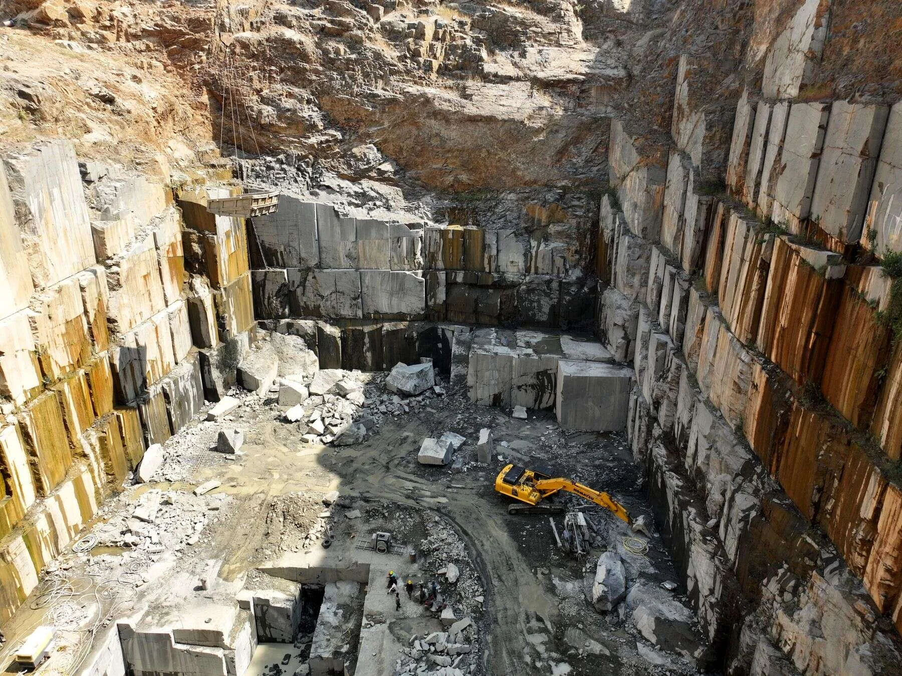Granite quarry pit with stacked stone walls and an excavator working below