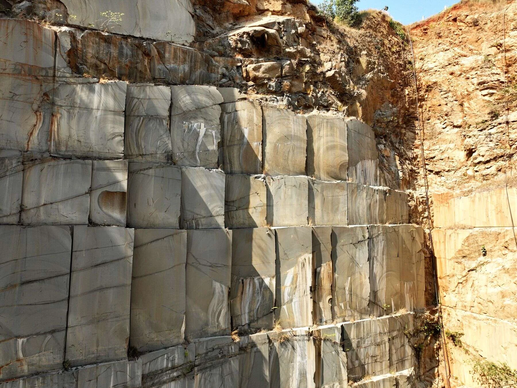 Sunlit granite quarry wall cut into neat rectangular blocks