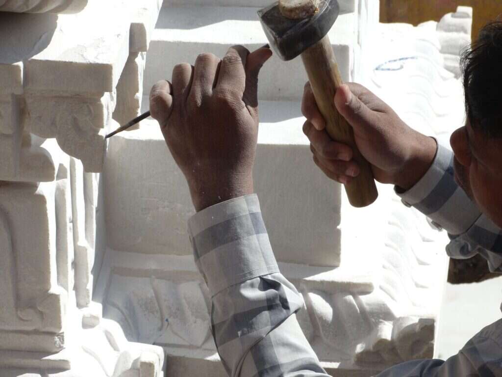 Hands carving white stone with chisel and hammer